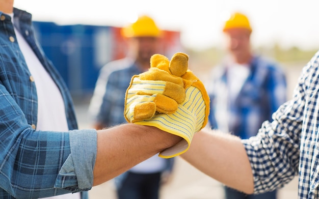 Gebouw, teamwork, partnerschap, gebaar en mensen concept - close-up van bouwers handen in handschoenen die elkaar begroeten met handdruk op bouwplaats