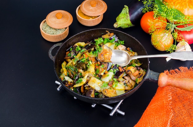 Gebraden aubergine, paprika en verschillende groenten in pan op zwarte achtergrond