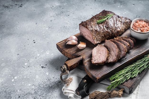 Gebraden en gesneden tri-tip biefstuk op een houten bord met kruiden Grijze achtergrond Bovenaanzicht Kopieer ruimte