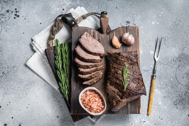 Gebraden en gesneden tri-tip biefstuk op een houten bord met kruiden. grijze achtergrond. bovenaanzicht.