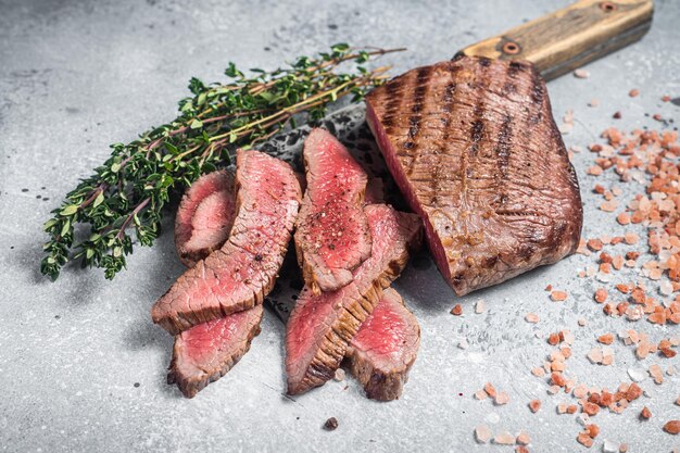 Gebraden gesneden Flank of Flap Steak op een slagersmes met tijm en roze zout Grijze achtergrond Bovenaanzicht