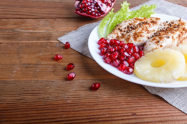 Gebraden kippenfilets met sla, ananas en granaatappelzaden op bruine houten achtergrond.