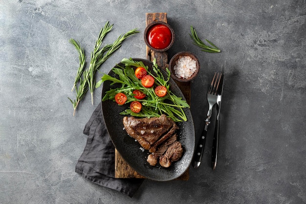 Foto gebraden rundvlees steak goed gedaan met verse groente salade en een glas licht bier op een zwarte plaat