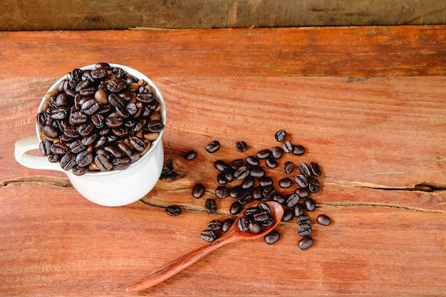 Gebrande koffiebonen in een koffiekop op houten vloer.