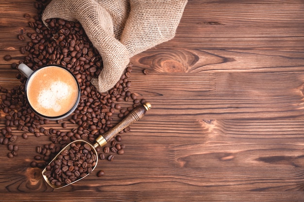 Gebrande koffiebonen wakker uit een jute koffiezak op een oude houten tafel.