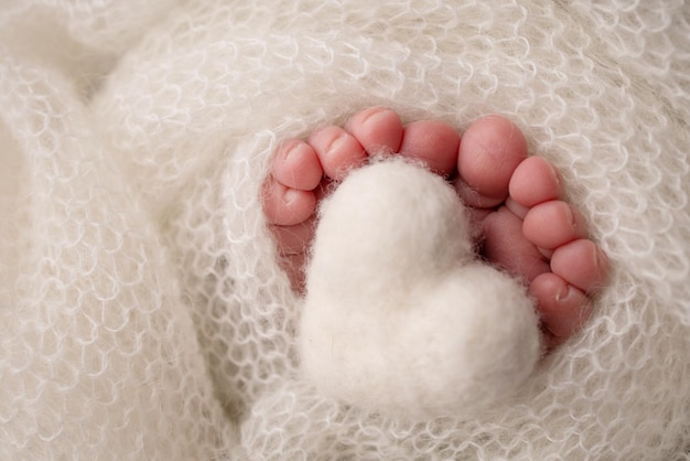 Gebreid wit hart in de benen van een baby Zachte voeten van een pasgeborene in een witte wollen deken Close-up van tenen, hakken en voeten van een pasgeborene Macrofotografie de kleine voet van een pasgeboren baby