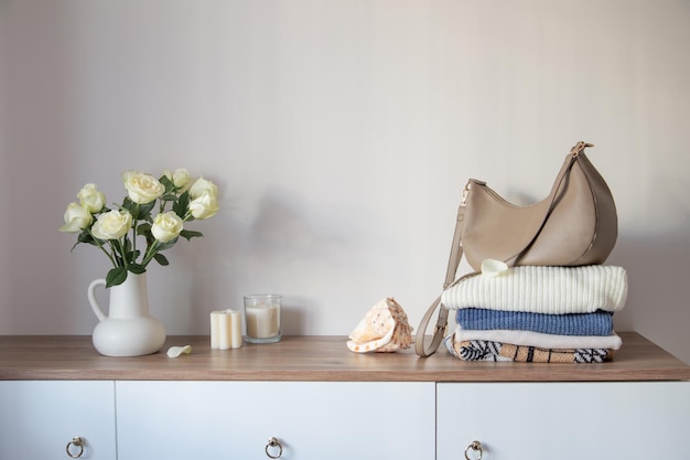 gebreide kleding en witte rozen in een kruik op een moderne dresser