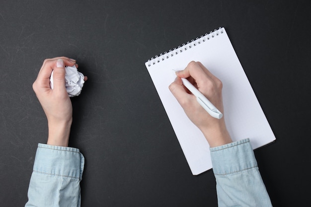 Gebrek aan ideeën. vrouwelijke handen schrijven in een notitieboekje en houden een proppen bal papier op een zwarte.