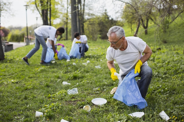 Gebrek aan respect voor de natuur. Positieve volwassen vrijwilliger die naar beneden kijkt en afval verzamelt