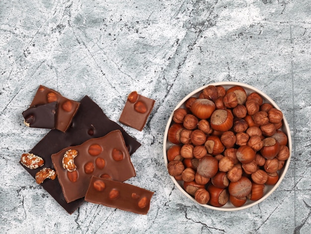 Foto gebroken chocoladerepen zoete cashewnoten en rauwe hazelnoten op grijze stenen achtergrond