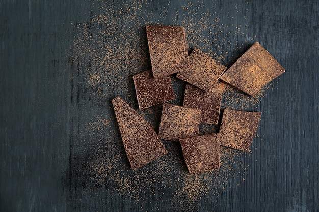 Gebroken chocoladestukken en cacaopoeder op zwarte achtergrond. Kopieer ruimte.