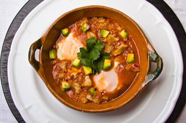 gebroken eieren, gerecht van gebroken eieren in tomatenbouillon vergezeld van varkenszwoerd en avocado op tafel