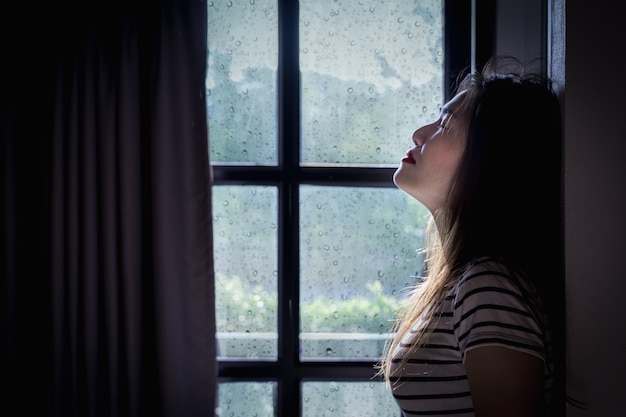 Gebroken hart jonge vrouw huilt in een donkere kamer met regenseizoen.