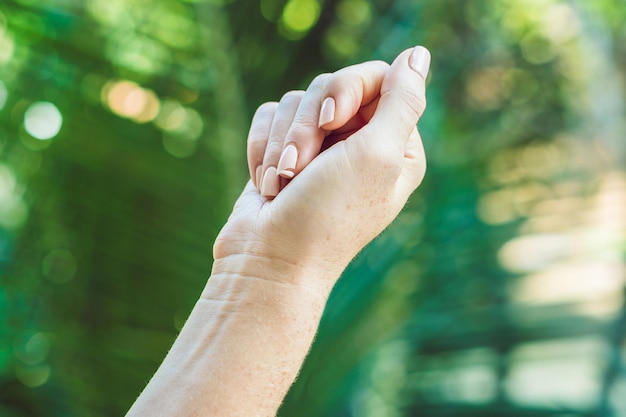 Gebroken nagel op de hand van een vrouw met een manicure op een groene achtergrond.