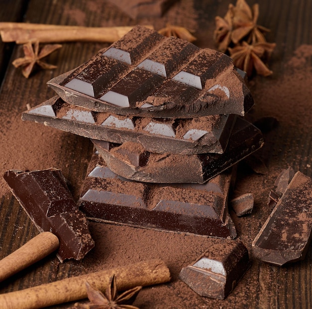 Gebroken stukjes donkere chocolade, kaneelstokjes en steranijs op een bruine houten tafel, bovenaanzicht