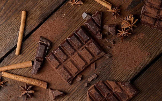 Gebroken stukjes donkere chocolade, kaneelstokjes en steranijs op een bruine houten tafel, bovenaanzicht