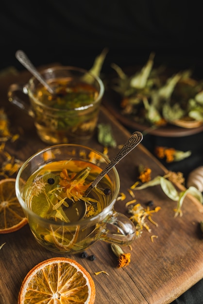 Foto gebrouwen kruidenthee in glazen bekers op een houten bord. kruidenthee ingrediënten. gedroogde munt, bosbessen, lindebloemen, merigold-bloem, calendula-bloemen.