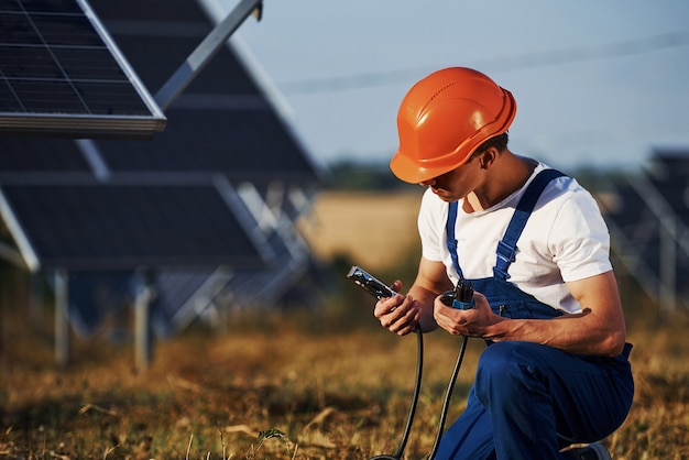 Gebruik van speciale apparatuur. Mannelijke werknemer in blauw uniform buitenshuis met zonnebatterijen op zonnige dag.