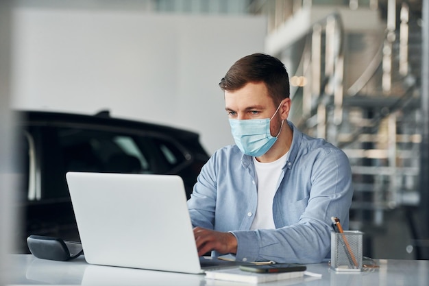 Gebruikt laptop Jonge man in wit overhemd en blauwe jas werkt binnenshuis