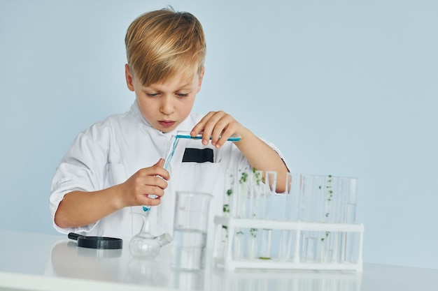 Gebruikt reageerbuizen Kleine jongen in jas die een wetenschapper speelt in het laboratorium met behulp van apparatuur