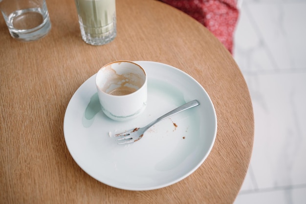 Gebruikte lege kop koffie met een witte vuile plaat en vork op houten tafel in een café na het drinken