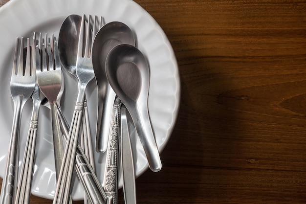 gebruikte zilveren vorken en lepels in verschillende uitvoeringen op een witte keramische plaat op houten tafel