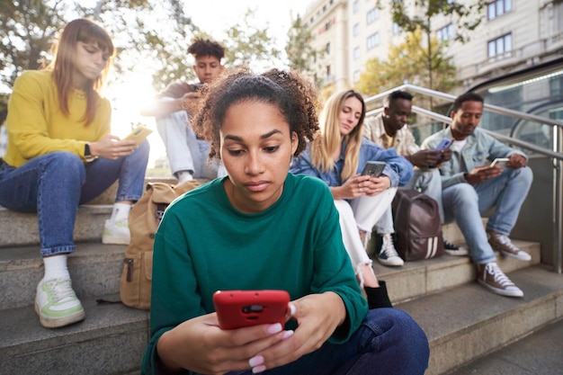 Geconcentreerd meisje kijkt en typt op haar telefoon zit op straat met vrienden techniek verslaafd