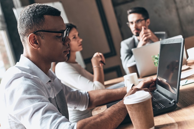 Geconcentreerd op het werk. Groep jonge moderne mensen in slimme vrijetijdskleding die werken terwijl ze in het creatieve kantoor zitten