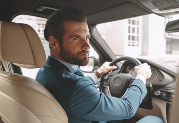 Geconcentreerd schattig mannetje in pak zittend in de salon van de auto