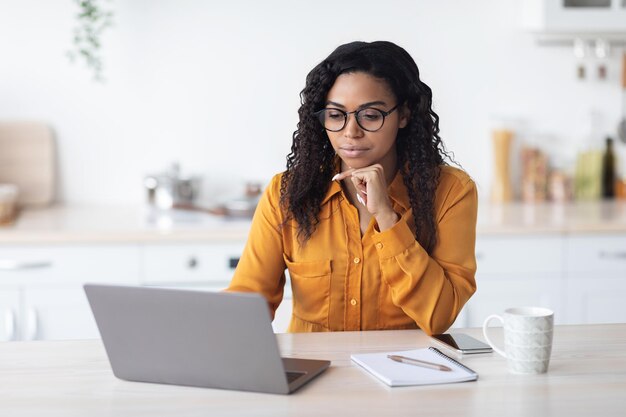 Geconcentreerde Afro-Amerikaanse vrouw freelancer met behulp van laptop thuis