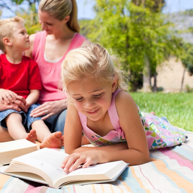 Foto geconcentreerde blonde meisjeslezing terwijl het hebben van een picknick met haar familie