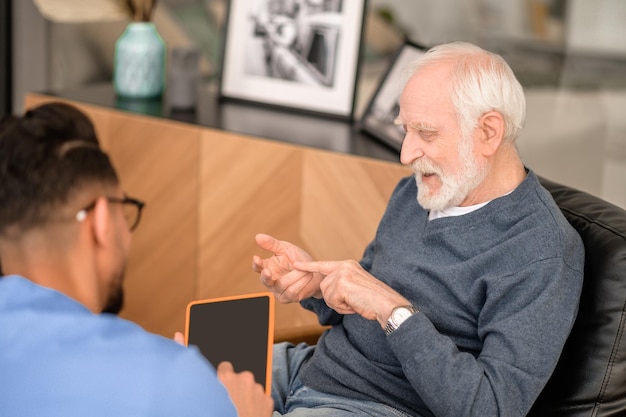 Geconcentreerde gepensioneerde die iets opsomt in gesprek met zijn verzorger