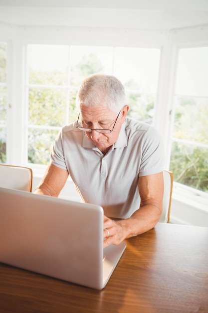 Geconcentreerde hogere mens die laptop thuis met behulp van