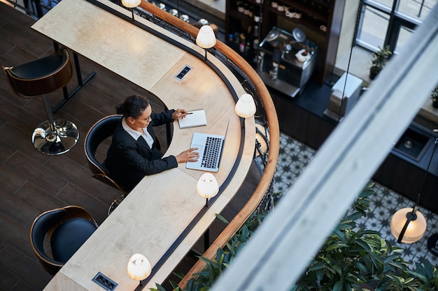 Geconcentreerde internationale vrouw die aan tafel zit terwijl ze aan haar computer werkt