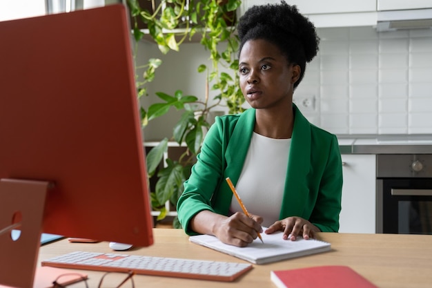 Geconcentreerde jonge Afrikaanse vrouw die op de computer in de keuken studeert en online werkt op kantoor aan huis