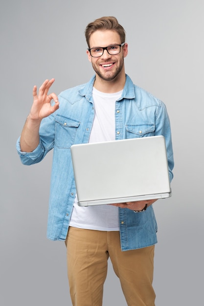 Geconcentreerde jonge bebaarde man met bril gekleed in jeans overhemd met laptop geïsoleerd