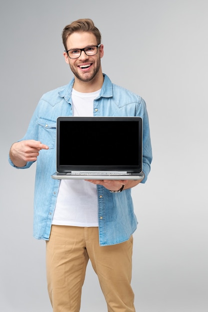 Geconcentreerde jonge bebaarde man met bril gekleed in jeans overhemd met laptop