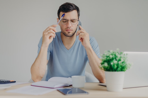 Geconcentreerde jonge mannelijke manager maakt internetproject, heeft telefoongesprek