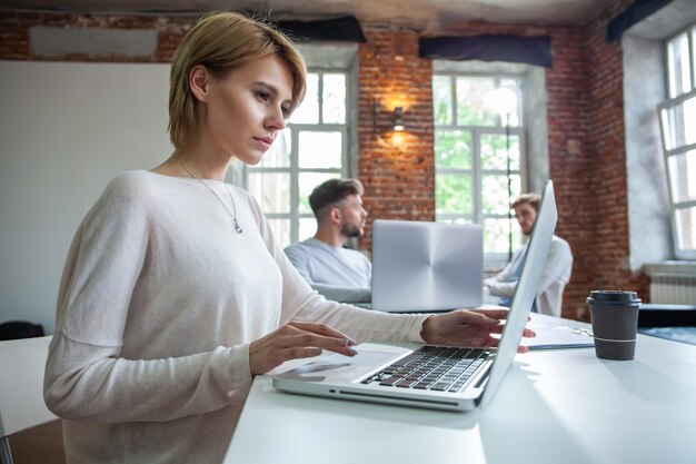 Geconcentreerde jonge mooie zakenvrouw die op laptop werkt in een helder modern kantoor.