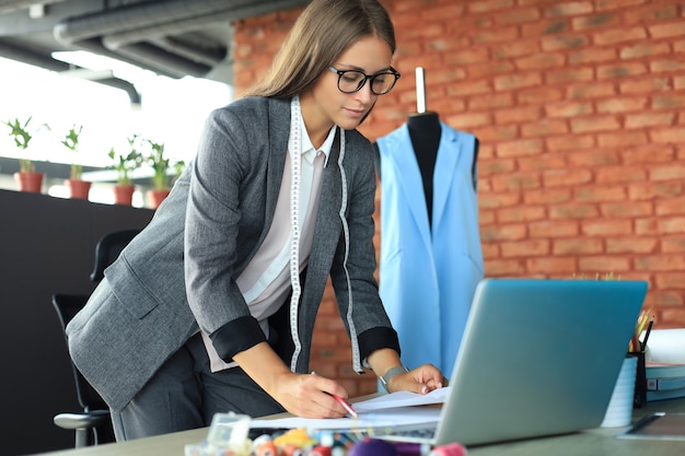 Geconcentreerde jonge vrouw die met laptop werkt terwijl ze in haar studio werkt.