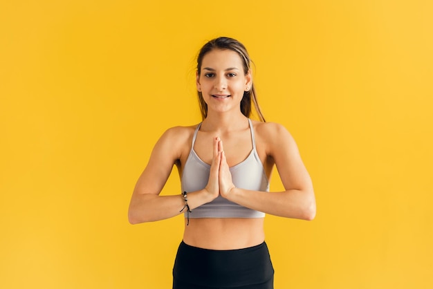 Geconcentreerde jonge vrouw in strakke sportkleding beoefenen van yoga hand in hand in namaste gebaar en mediteren ontspannen kijken naar camera Vrouw bidden en hand in hand in zen op gele achtergrond