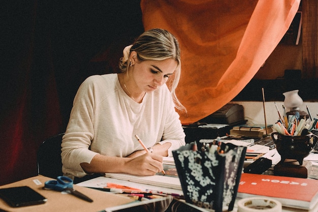 Geconcentreerde jonge vrouwelijke tekening met potlood op de werktafel met verschillende kunstobjecten