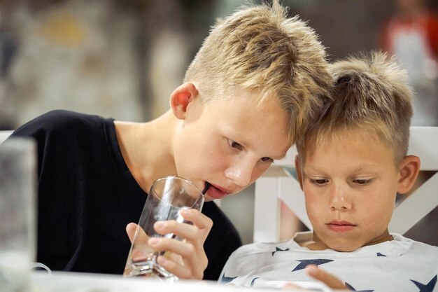 Foto geconcentreerde jongens bekijken video op mobiele telefoon en drinken drank in restaurant vriendelijke kinderen