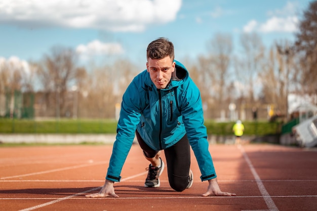 Geconcentreerde knappe jonge sportman die zich voorbereidt om te beginnen met rennen op tartanbaan in het stadion.