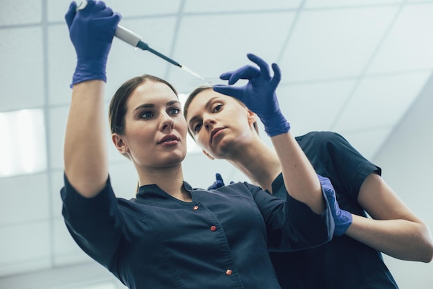 Geconcentreerde laboranten kijken naar het microscoopglaasje en een vrouw die een automatische pipetdispenser gebruikt