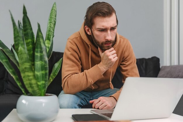 Geconcentreerde man die thuis werkt en naar laptop kijkt