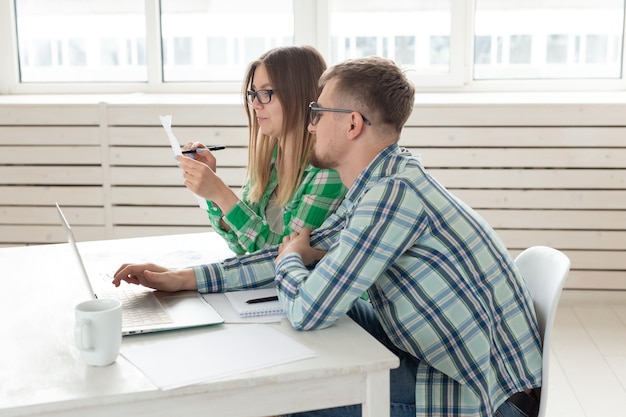 Geconcentreerde man en vrouw tellen aankopen en rekeningen van de afgelopen maand en leggen de resultaten vast in hun huisboekhouding in een notitieboekje en op een laptop. Concept van sparen en boekhouding.