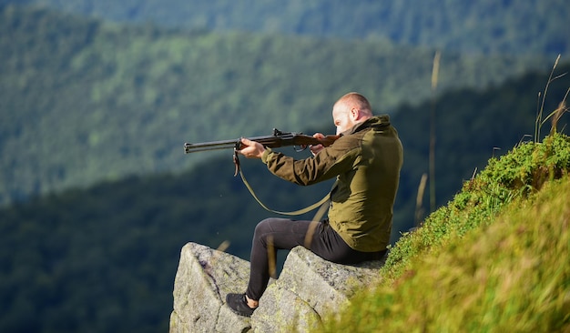 Geconcentreerde man klaar om jager te vuren hobby militair mannetje in camouflage soldaat in het veld veelhoek leger kracht sluipschutter bereik doel berg gespierde man houd wapen doel en succes vast