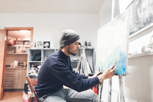 Geconcentreerde man staat in een studio bij het canvas en schetst een foto