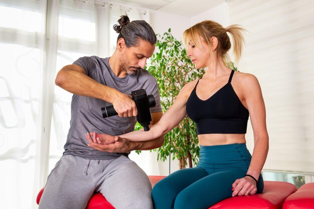 Foto geconcentreerde massagetherapeut met behulp van een massagepistool op de cliënt